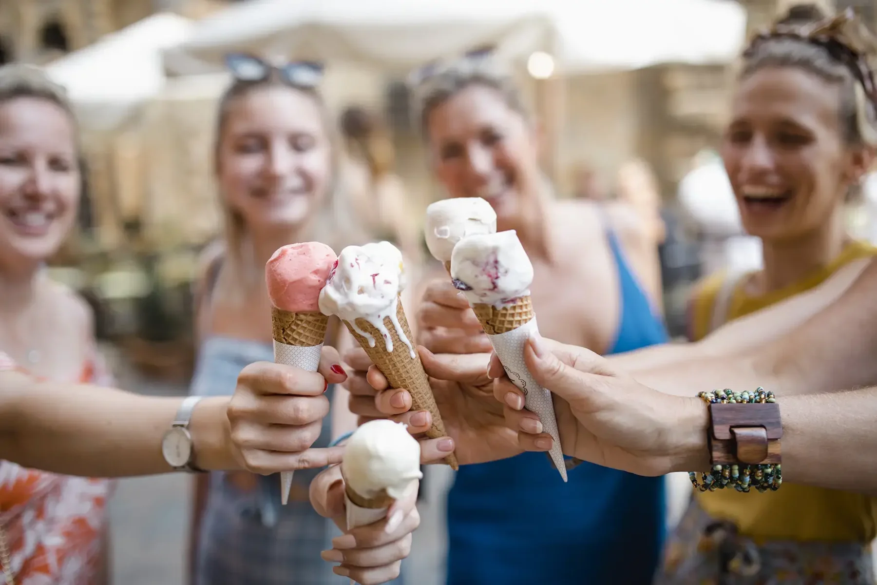 Friends in an outdoor market touching ice cream cones together in a circle